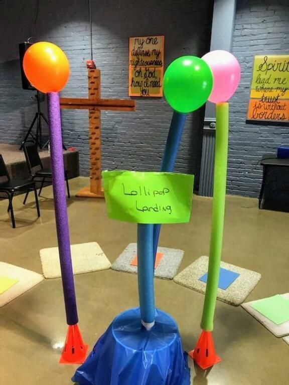 Balloon-decorated cross with a green sign in a dim indoor display area