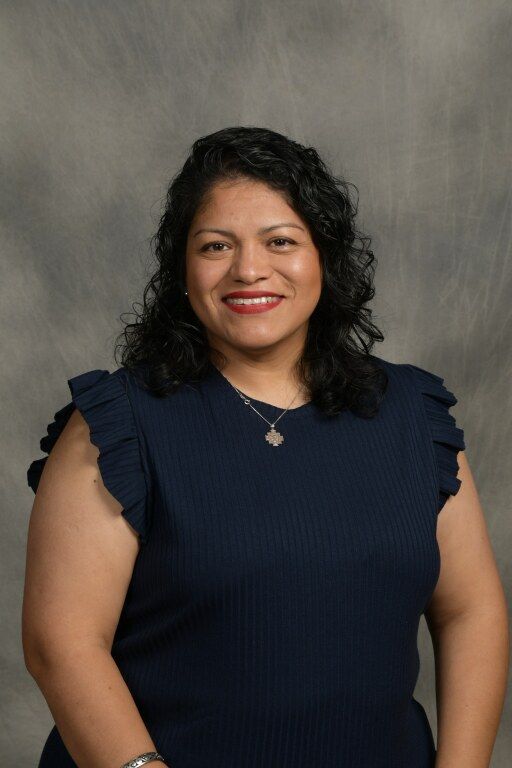 Woman in a navy sleeveless top smiling against a gray studio backdrop