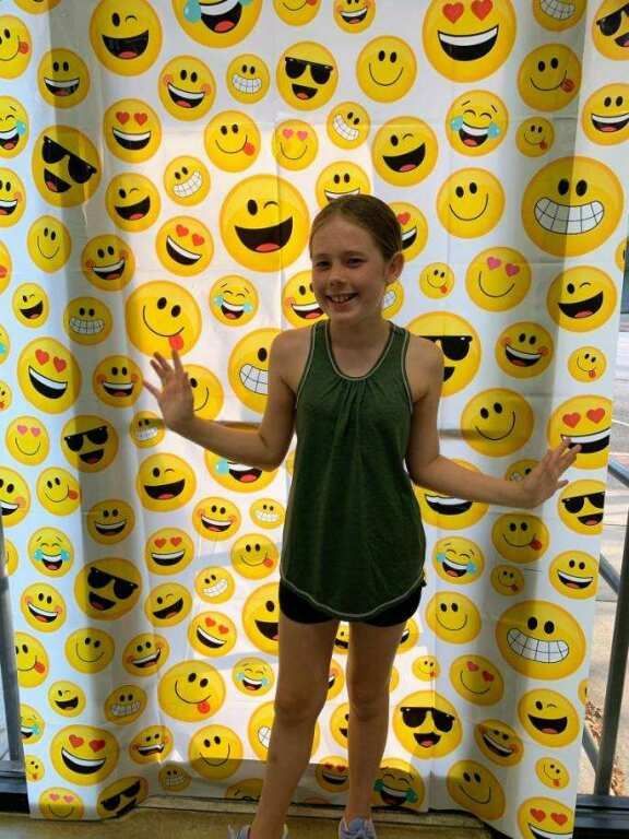 Person standing in front of a smiley-face backdrop, holding small props and smiling