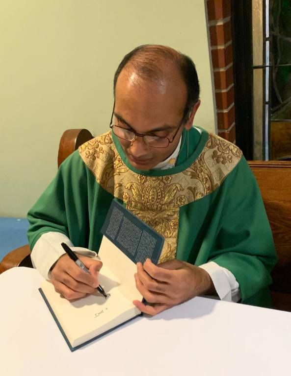 Man in a green and gold robe signing an open book at a table