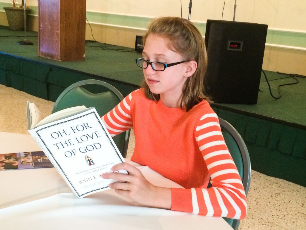 Person in orange striped shirt reading a booklet at a table in a classroom setting