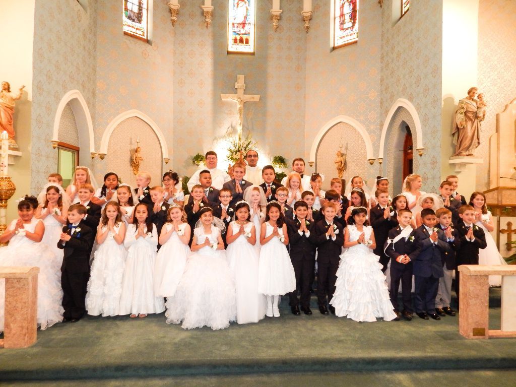 Large group posed in white dresses and dark suits in a church before an altar and cross