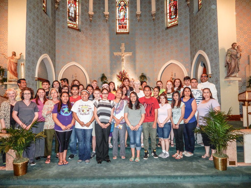 Large group posing inside a church sanctuary beneath stained glass windows and a cross