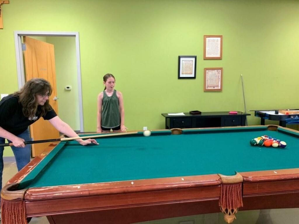 Two people lining up a shot at a pool table in a green game room