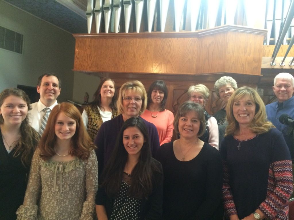 Group of people posing indoors in front of a wooden wall, smiling at the camera.