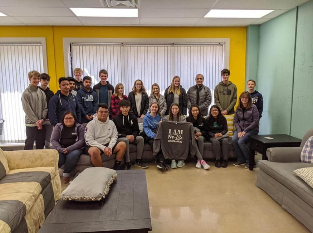 Group of people posing in a bright lounge with yellow and teal walls and large windows.
