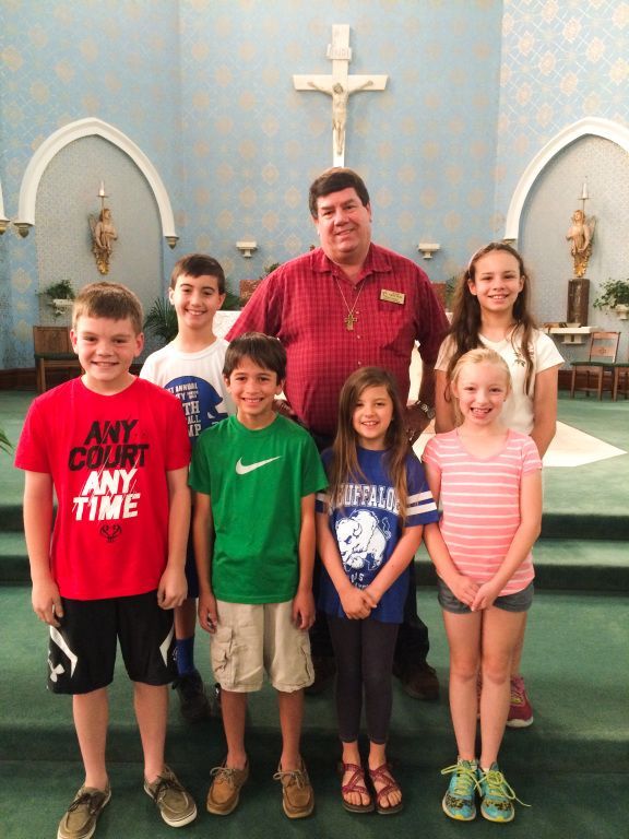 Group posing in a church with a priest, standing before an altar and cross.