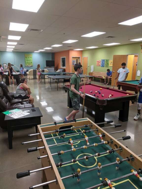 Recreation room with people playing pool and foosball under bright ceiling lights