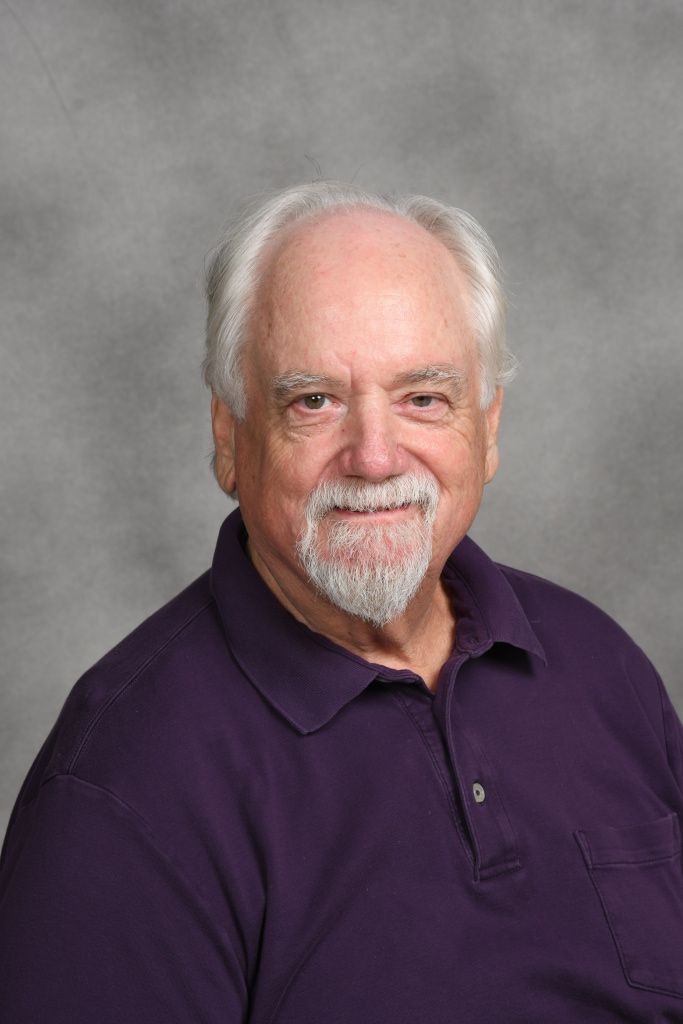 Portrait of a smiling man in a purple polo against a gray studio backdrop
