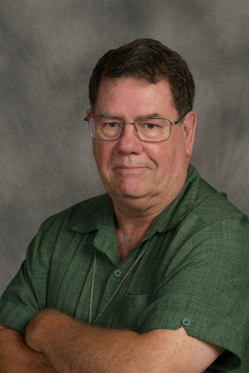 Portrait of a man in glasses and a green shirt with folded arms against a gray backdrop