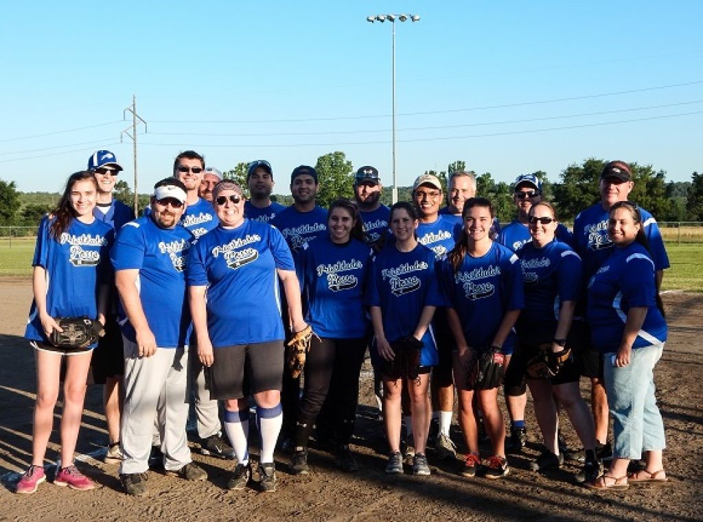 Youth softball team in blue shirts posing together on a dirt field outdoors