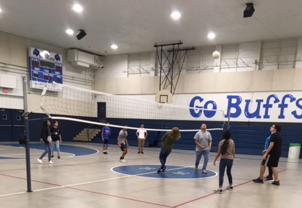 People playing volleyball in a gym with blue and white walls and a “Go Buffs” banner.