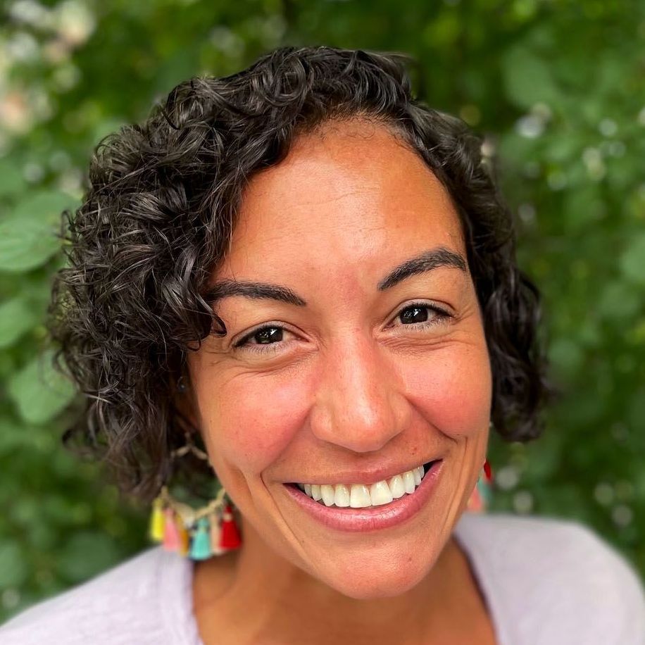 A woman with curly hair and earrings is smiling for the camera.