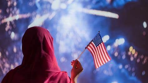 Woman in traditional garb holding an American flag watching fireworks.