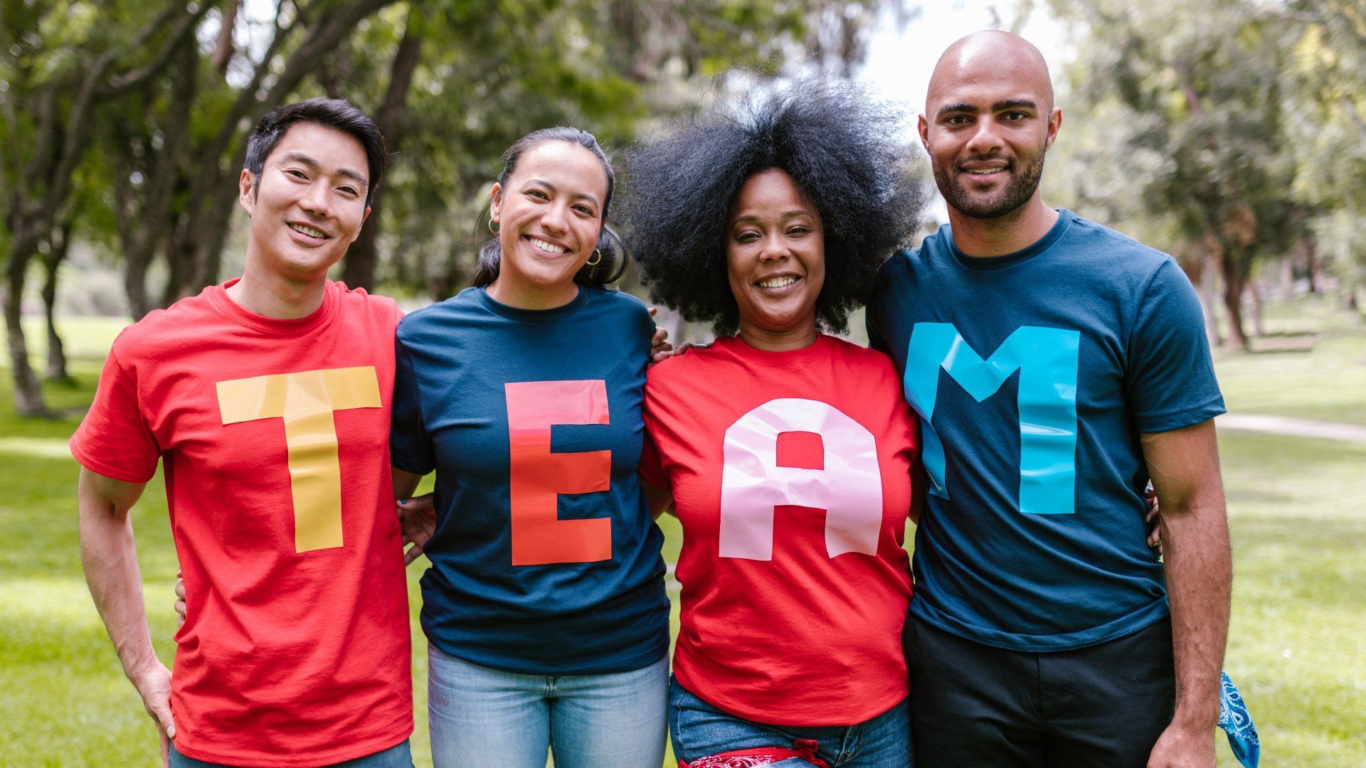 4 people are standing side by side, letters on their shirts spell, TEAM.