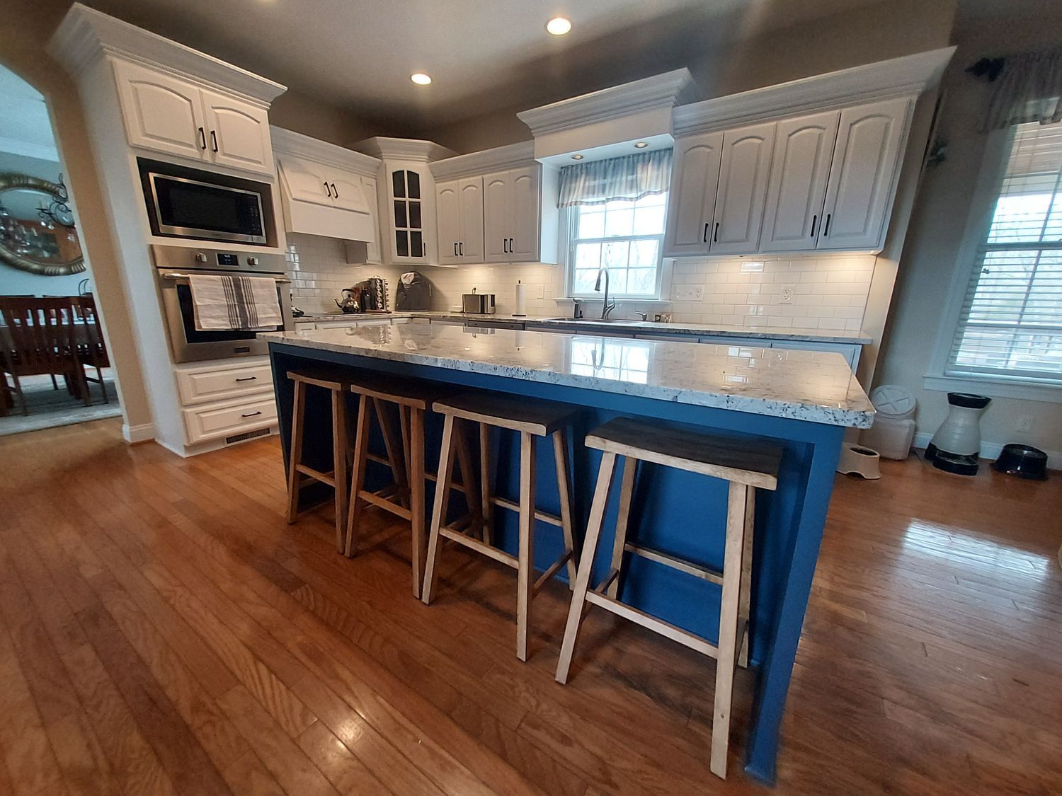 A kitchen with white cabinets and a blue island with stools.
