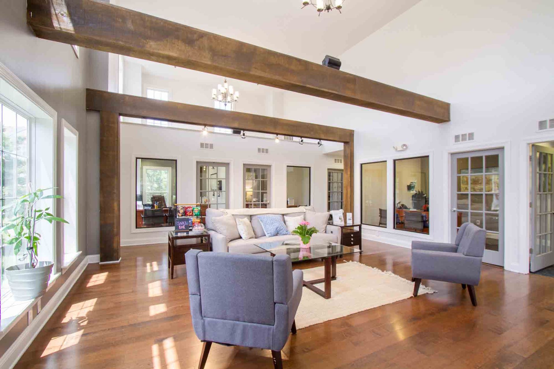 Lounge area with light gray walls, hardwood floor, two blue armchairs, sofa, coffee table, and large wooden beams at Hamburg Farms, offers apartments in Lexington, KY.