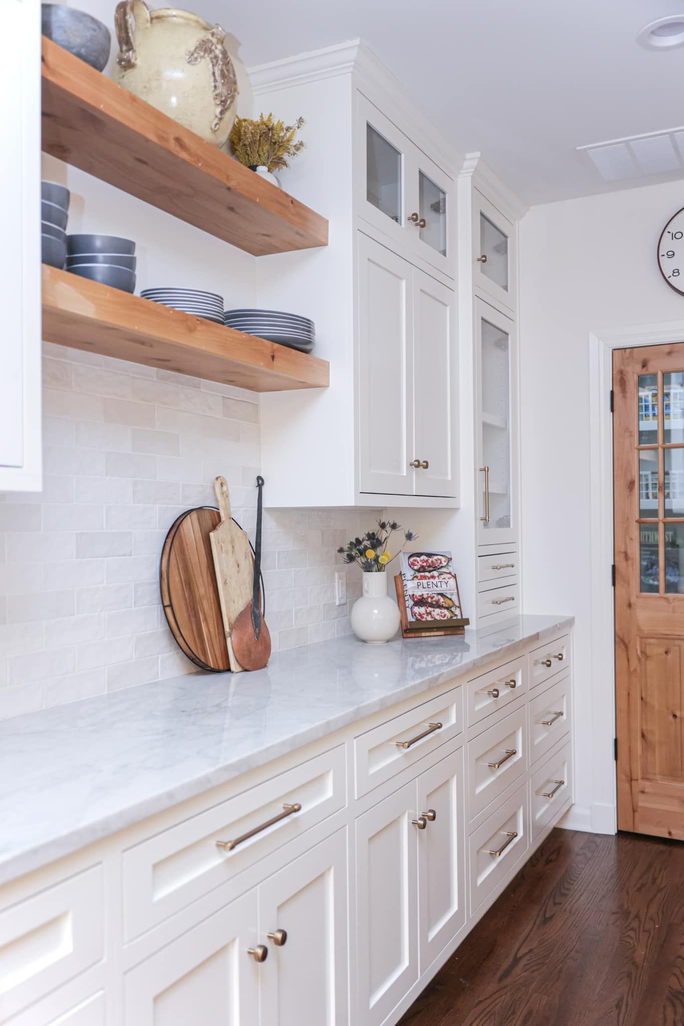 A kitchen with white cabinets , marble counter tops , and wooden shelves.