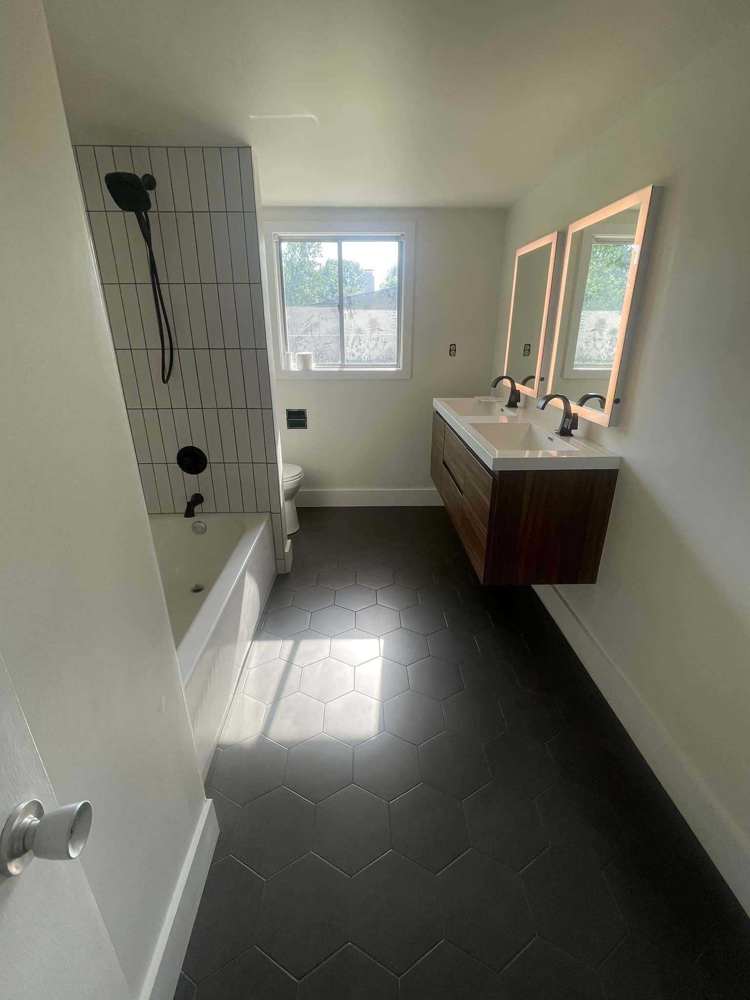 A bathroom with two sinks , a tub , and two mirrors.