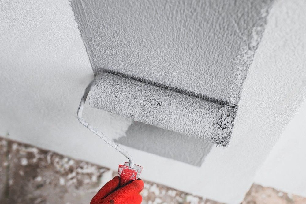 A painter applies gray paint to the exterior wall of a building using a paint roller.