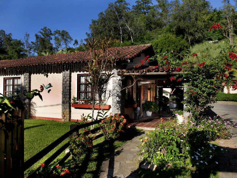 Uma casa com telhado de telha vermelha é cercada por árvores e flores