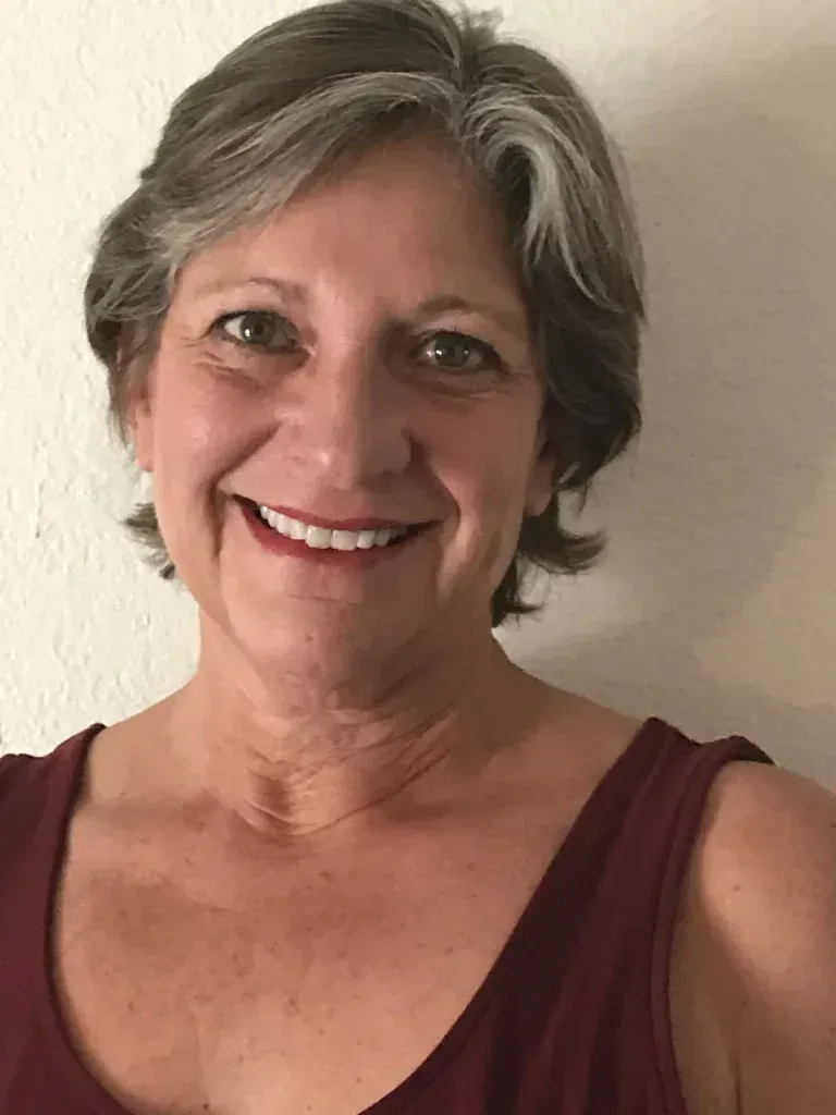 Woman with short gray hair smiles in a maroon tank top.