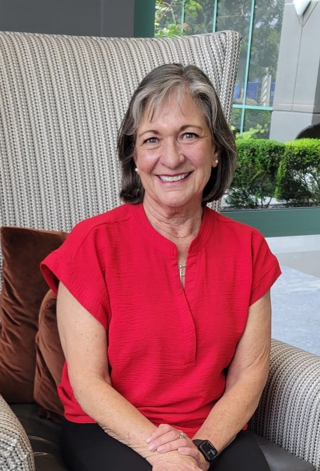 Woman with short gray hair smiles in a maroon tank top.