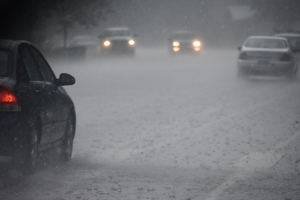 Cars driving on a rain-soaked road with limited visibility, headlights on.