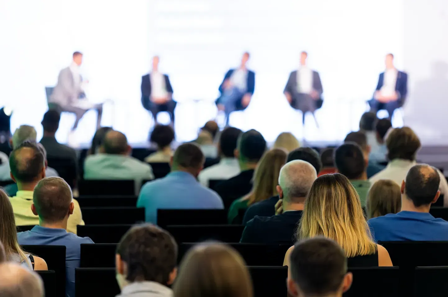 A large group of people are sitting in an auditorium watching a presentation.