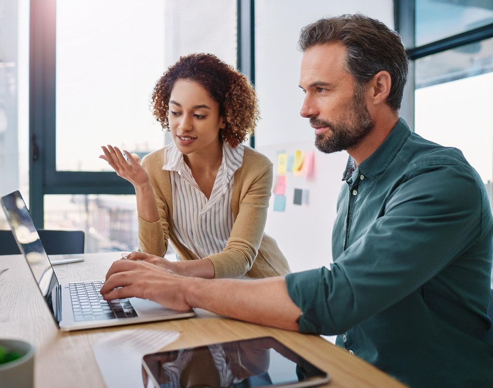 A man and a woman are sitting at a table looking at a laptop computer designing a website.