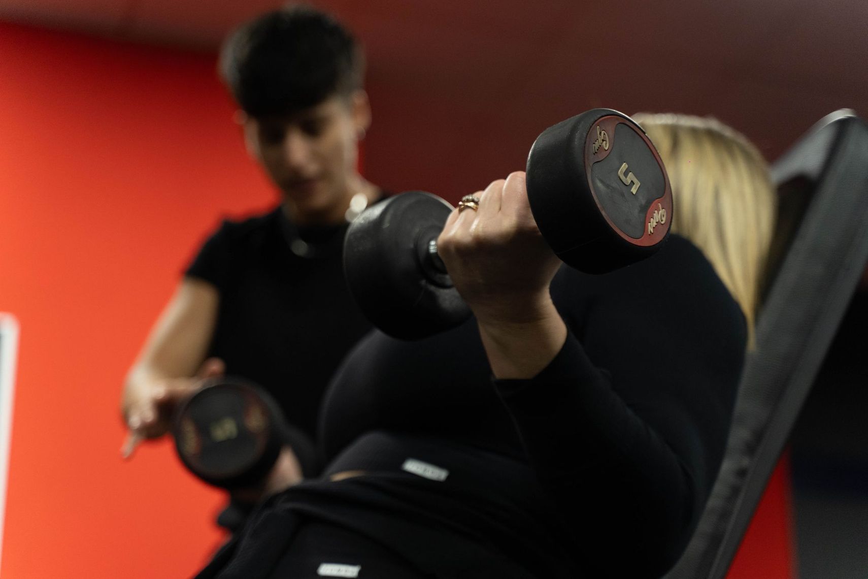 Donna sorridente su un tapis roulant, indossa abiti sportivi neri con il logo
