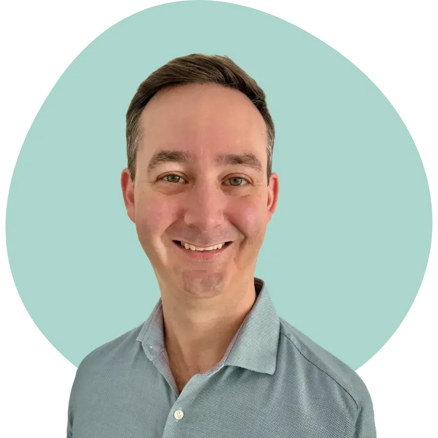 Smiling person in a light blue shirt against a pale teal background