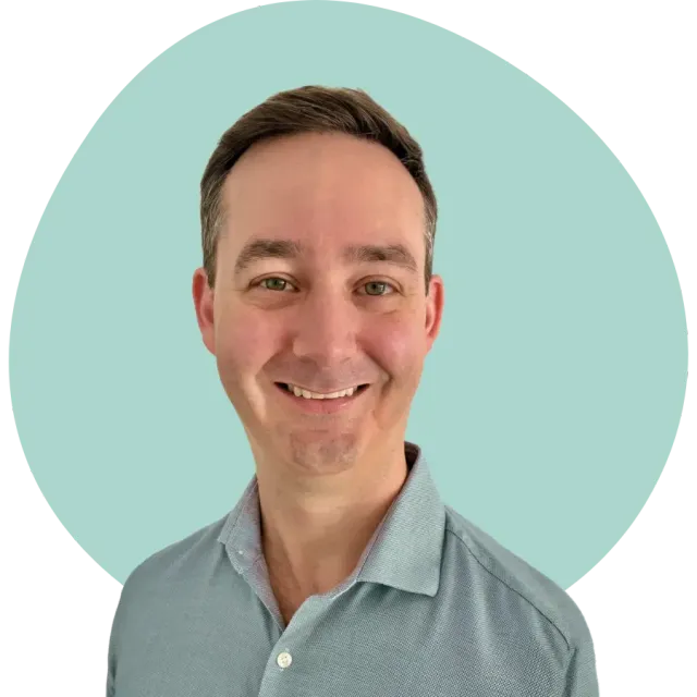 Smiling person in a light blue shirt against a pale teal background
