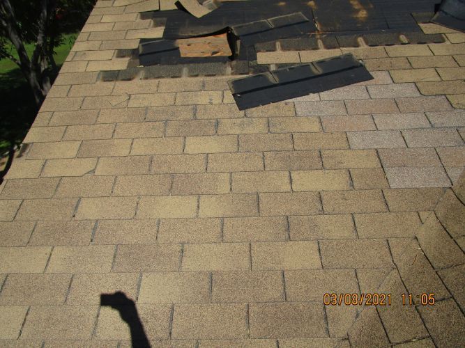 A roof with shingles missing and a hole in it