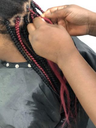 Hands braiding hair with red and black extensions.