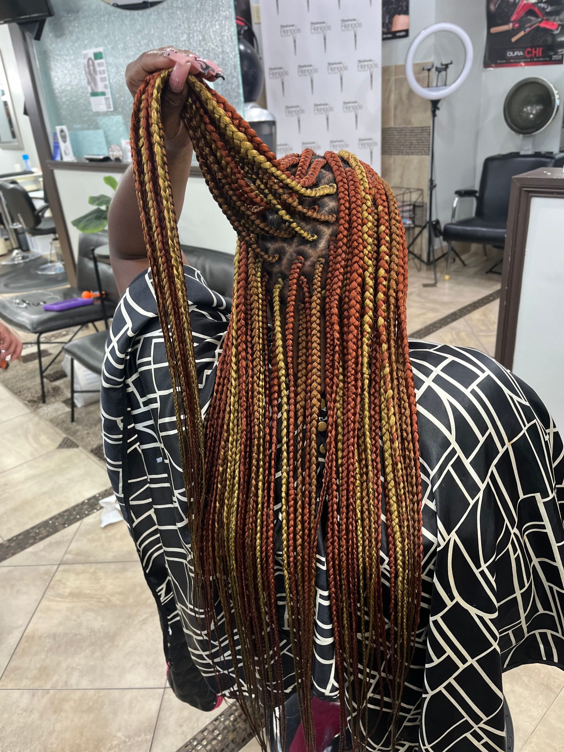 Person with long, reddish-brown and gold braids in a salon, holding up some of the braids.