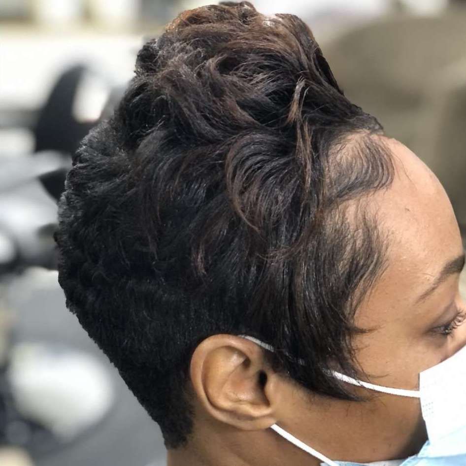 Woman with short, dark, textured hairstyle, wearing a white face mask, with hair styled up and to the side.