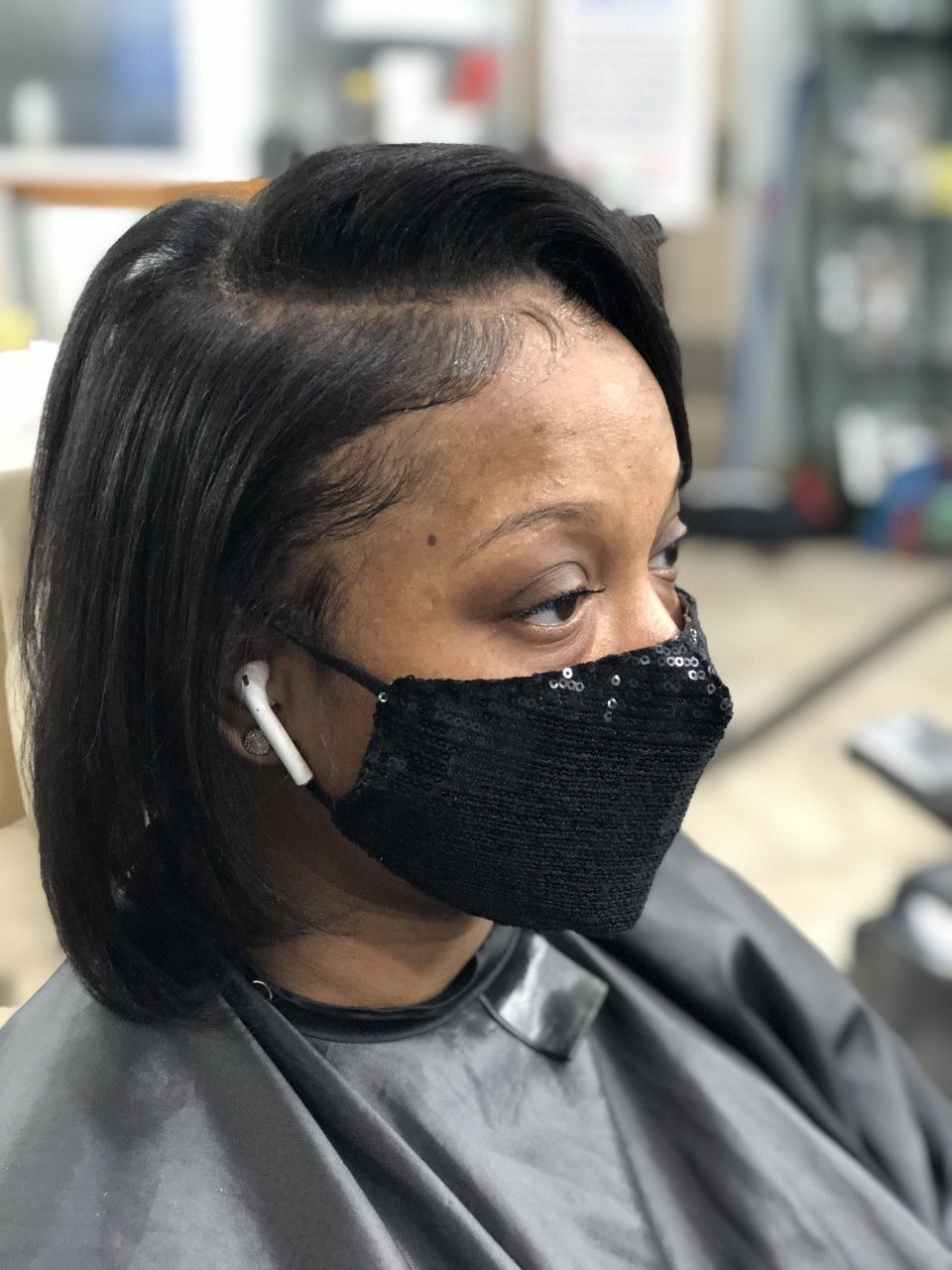 Woman with short, sleek, dark hair and black sequin face mask. In a salon setting.