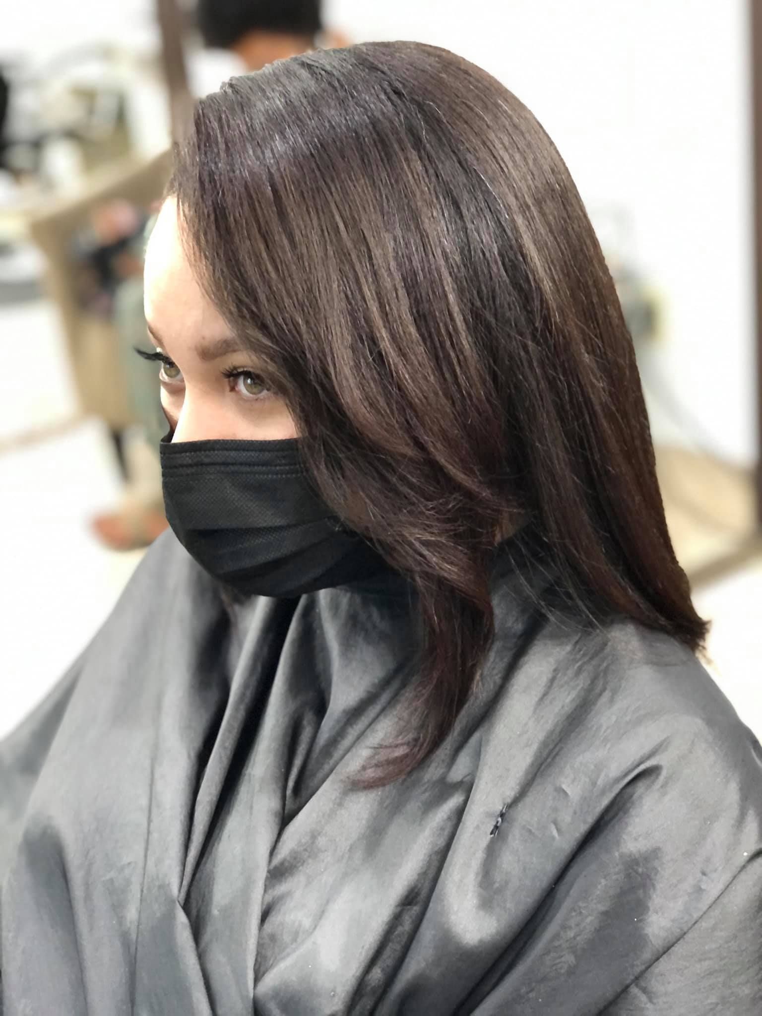 Person with dark hair wearing a black face mask, in a salon, hair styled.