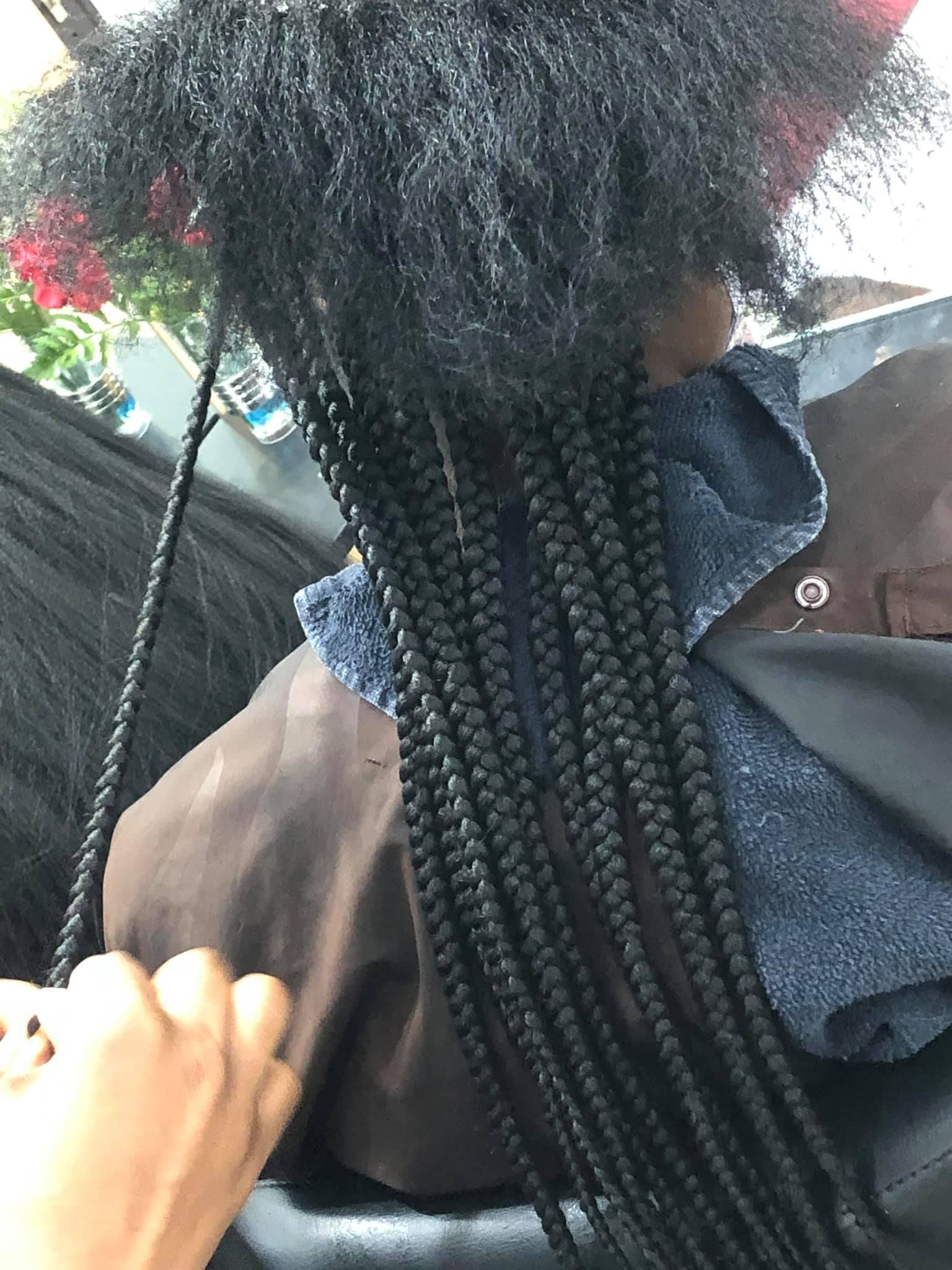 Person getting long black braids, hair partly unbraided at the top, a hand is visible.