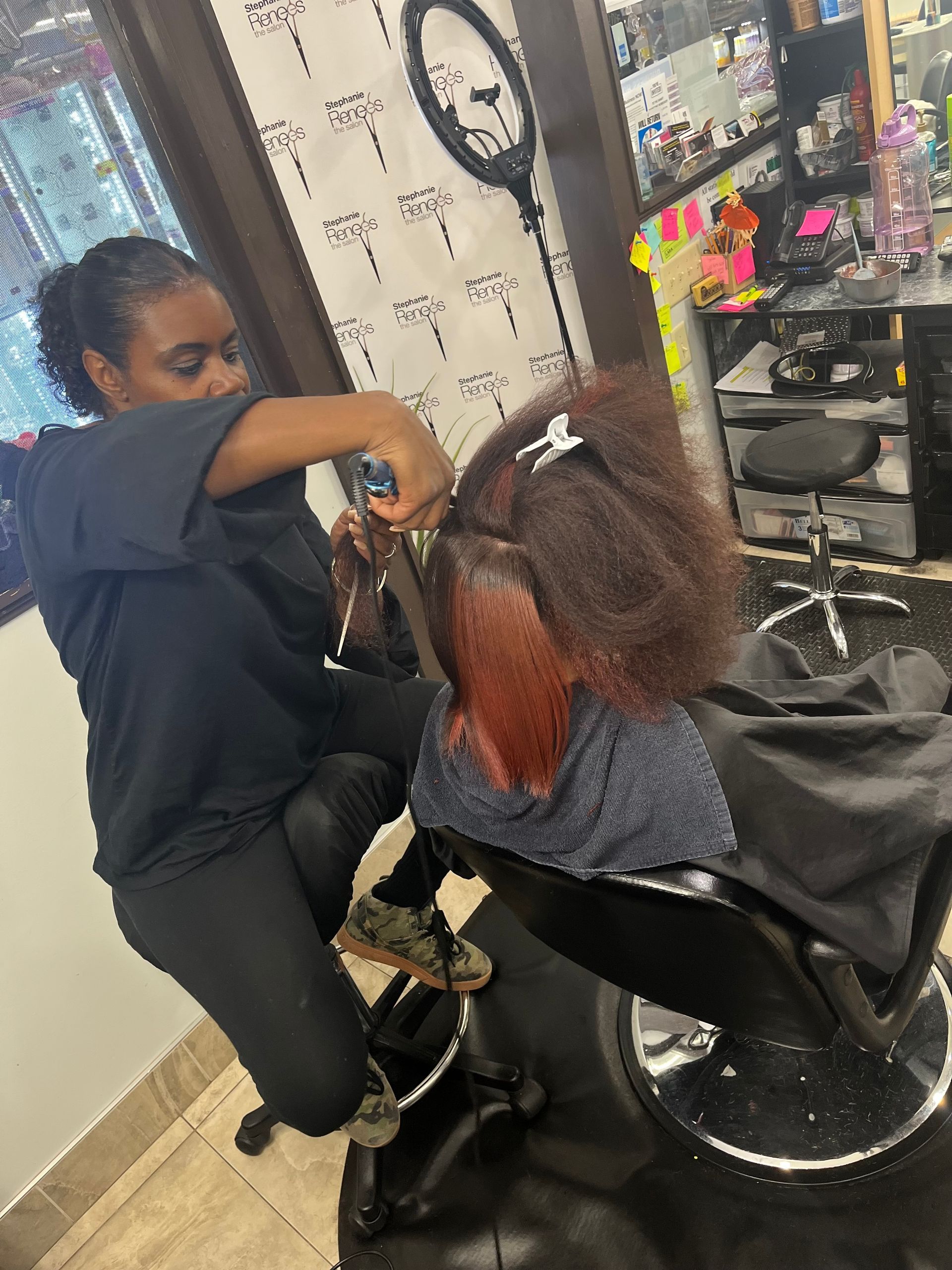 A person cutting hair in a salon. They are holding scissors and spraying water on a head with reddish-brown hair.