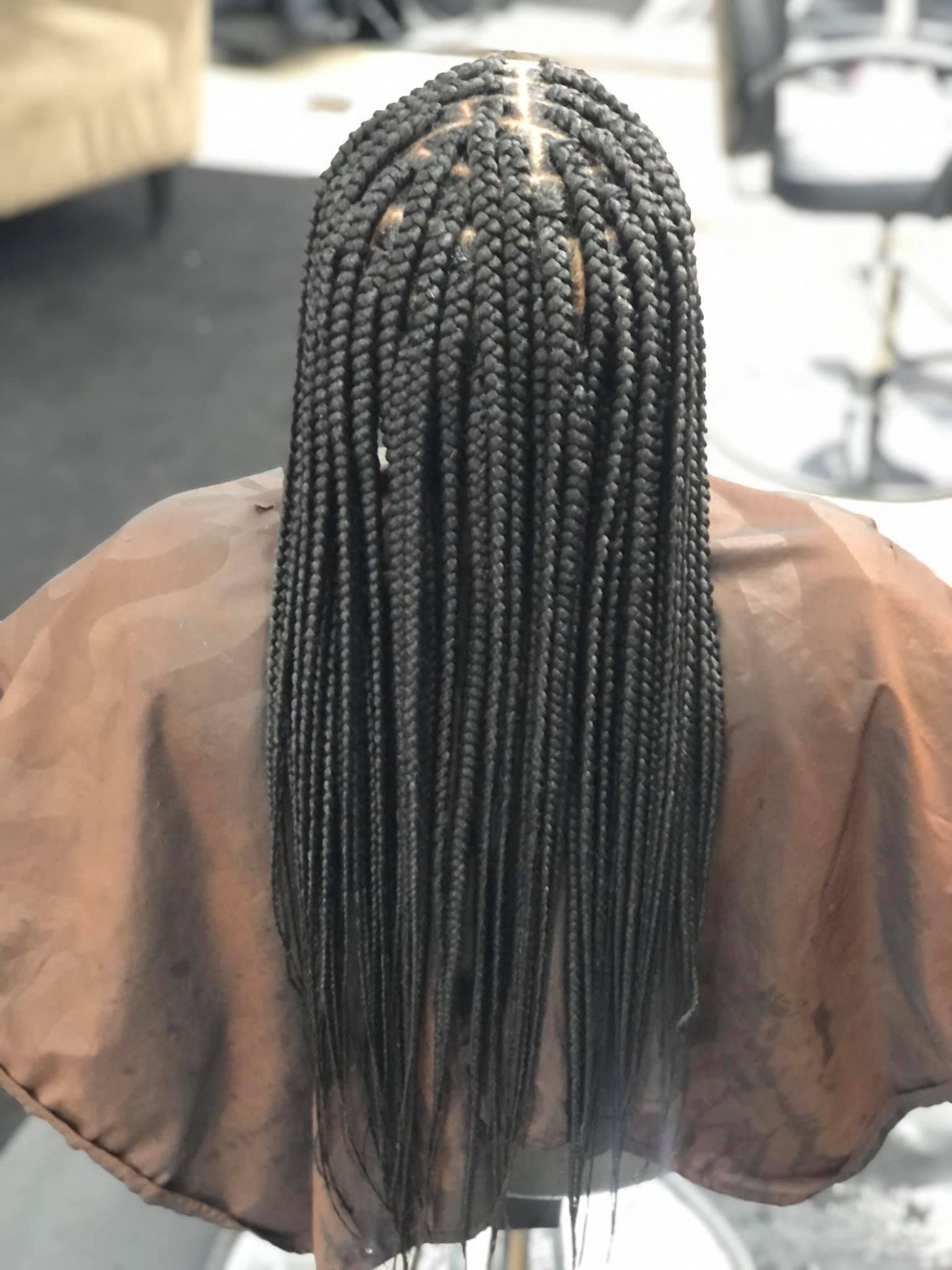 Back view of a person with long black box braids, wearing a brown salon cape.
