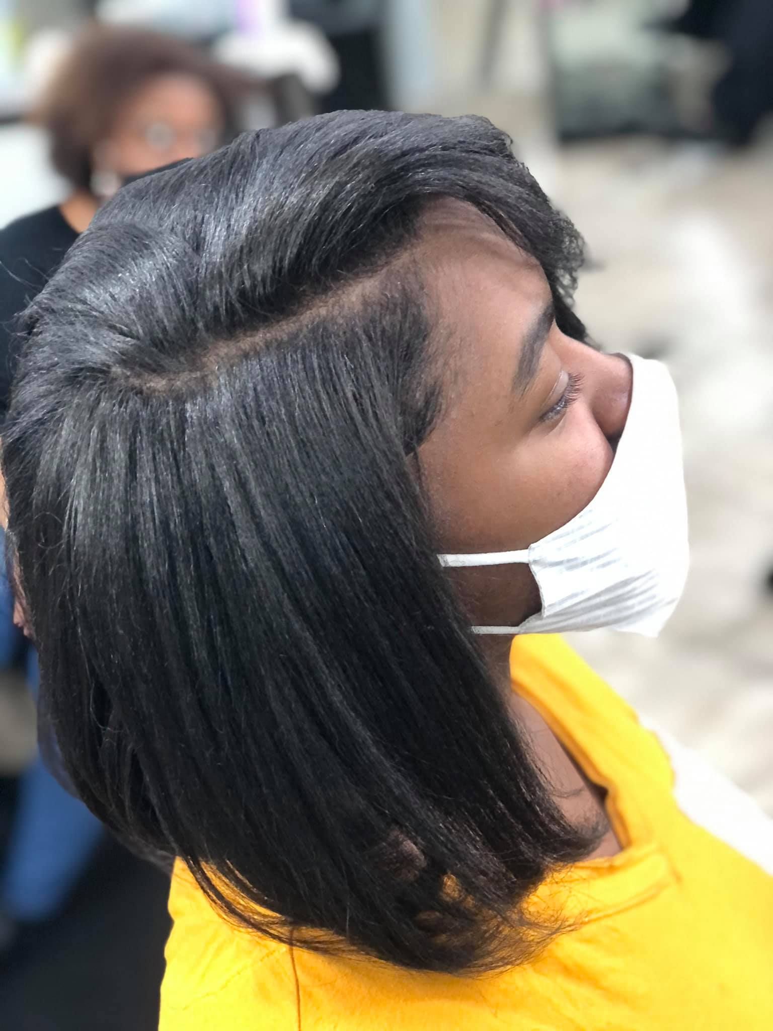 Person with straight, black hair wearing a face mask in a salon.