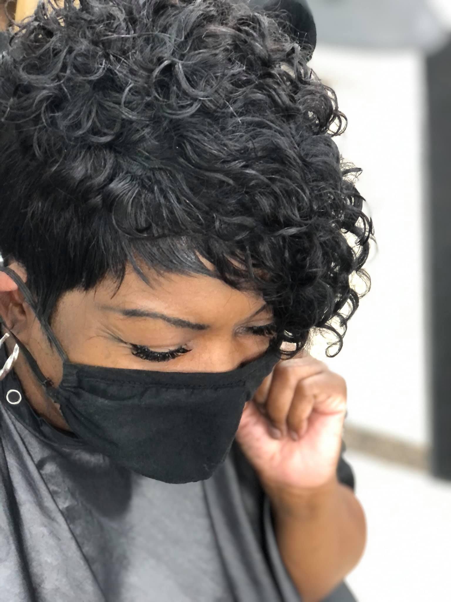 Woman with short, curly black hair, wearing a black mask and salon cape.