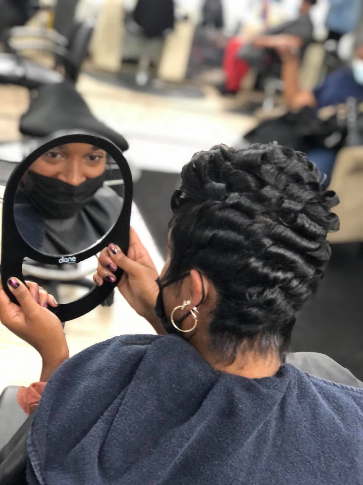 Person in salon checks new hairstyle in mirror, black hair styled in waves.