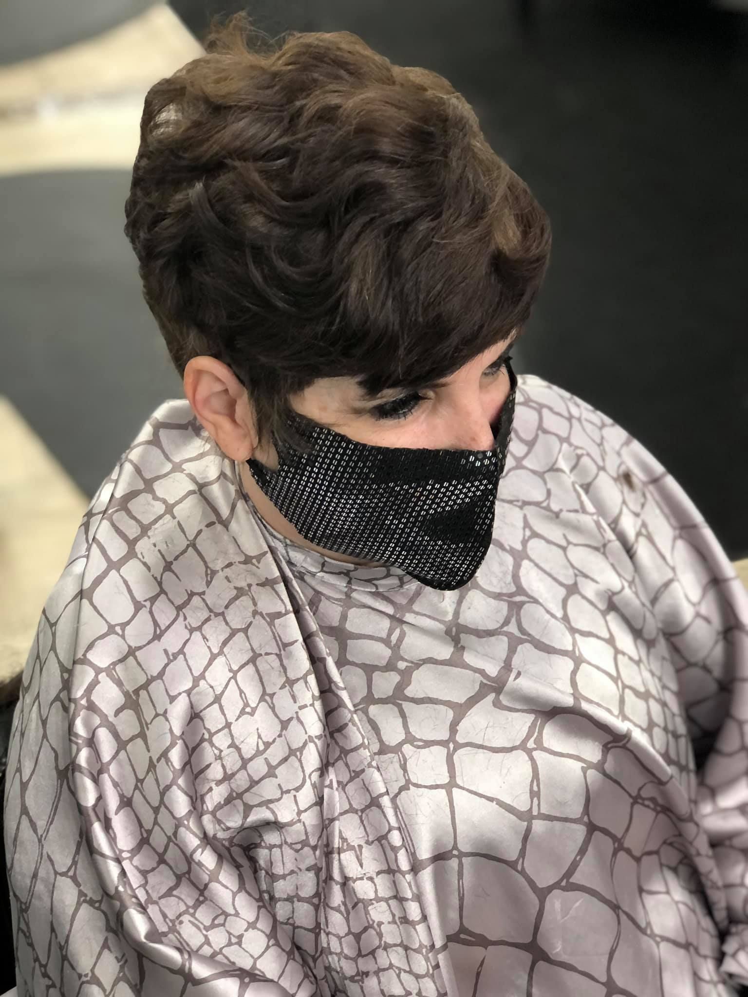 Person wearing a face mask and a patterned smock with brown hairstyle in a salon.