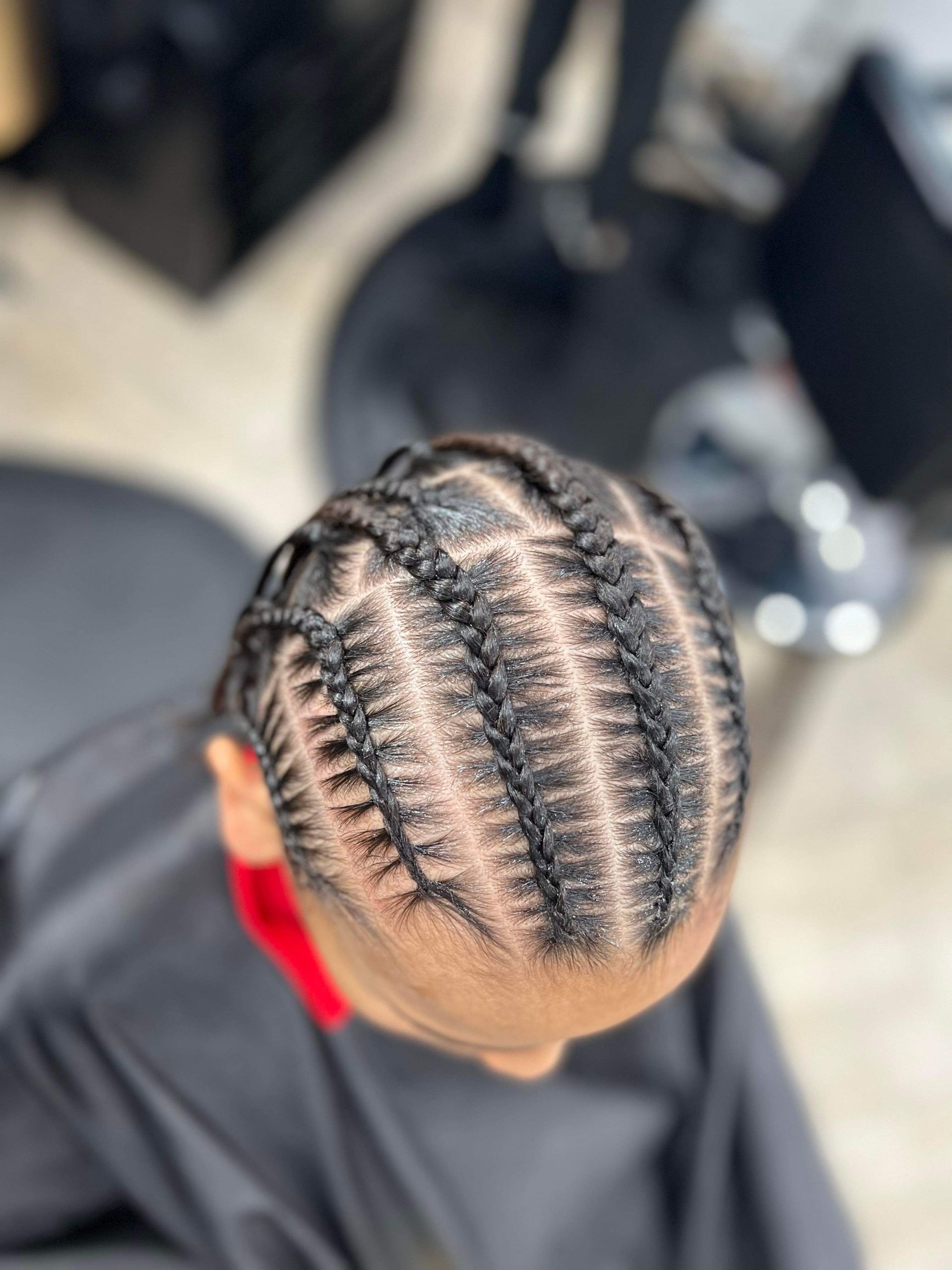 Close-up overhead view of a person's head with neatly braided cornrows in a salon setting.