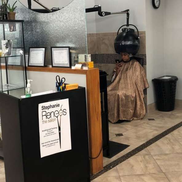 Hair salon interior: person under hooded dryer, receptionist desk, display shelf, waiting area.