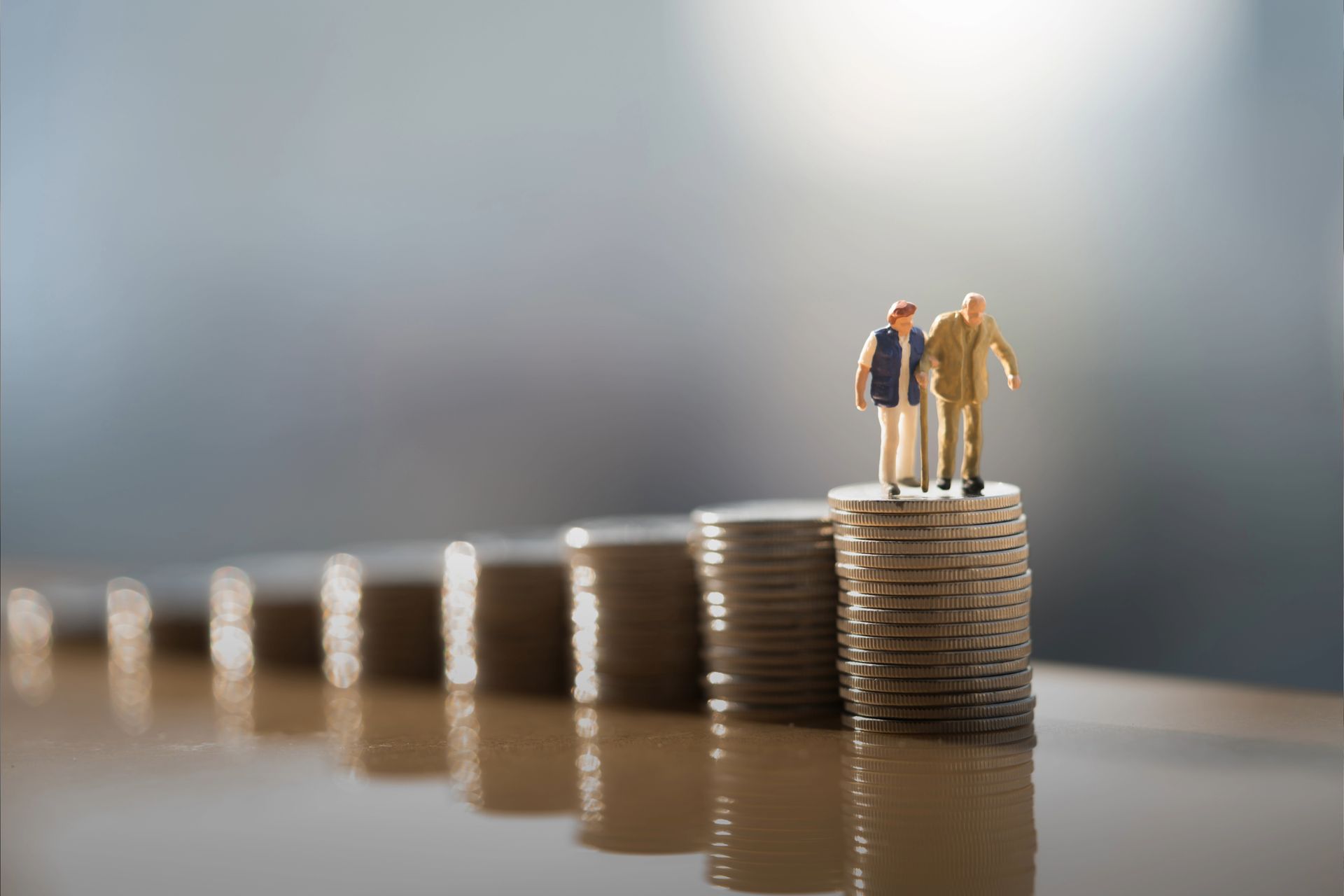 Miniature elderly couple standing on a stack of coins, symbolizing retirement or savings progress.