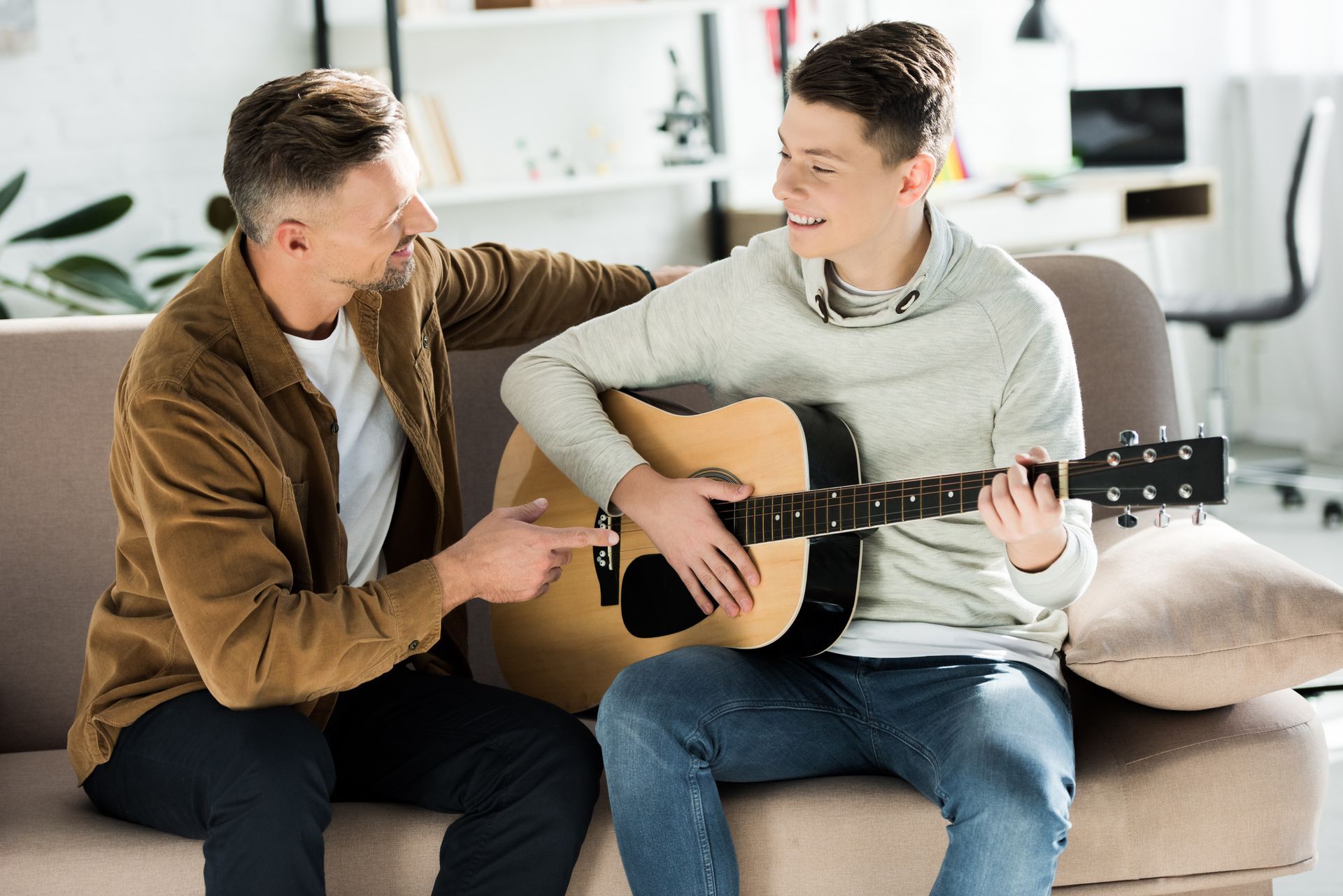 a father and son are sitting on a couch playing guitar
